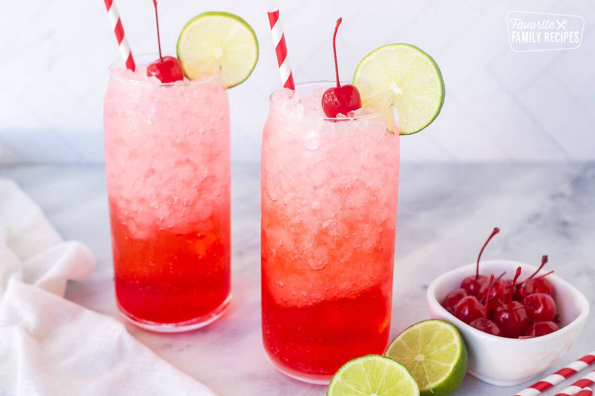 Two tall glasses of Shirley Temple Drinks garnished with lime slices and cherries.