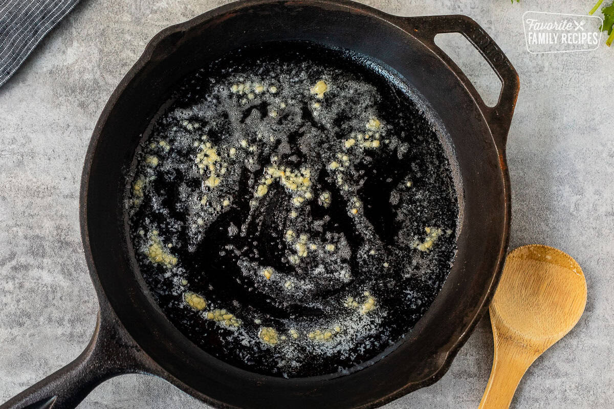 Skillet with melted butter and garlic. Wooden spoon on the side.