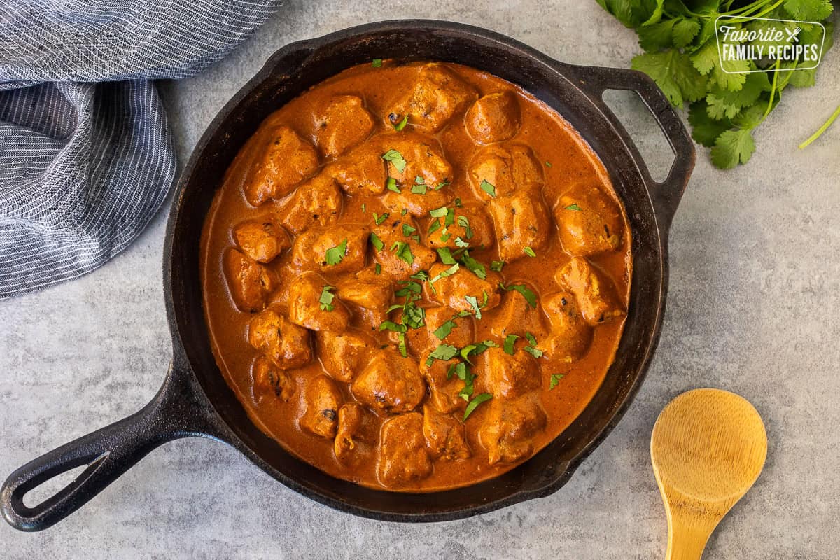 Chicken Tikka Masala in skillet garnished with cilantro. Wooden spoon on side.