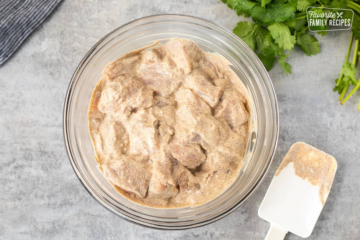 Glass bowl with chicken pieces marinating in yogurt, lemon, cumin, garam masala, and other spices