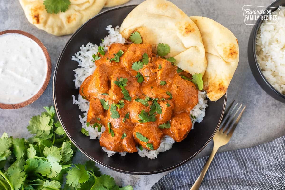 Chicken Tikka Masala over rice in a bowl garnished with cilantro and Naan bread resting on the side.