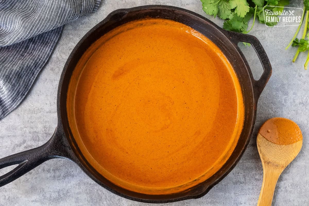 Skillet with chicken tikka masala sauce and wooden spoon on the side.