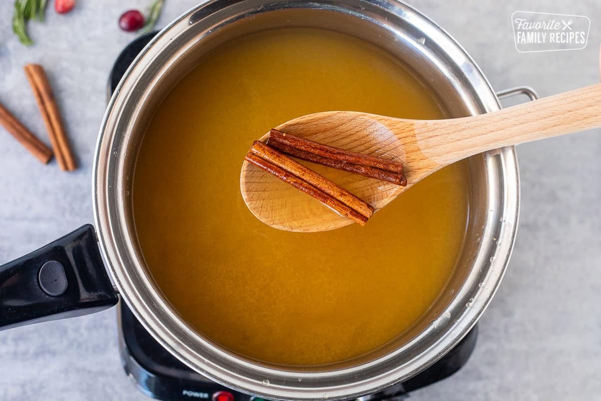 Saucepan with two cinnamon sticks in apple cider and a wooden spoon.