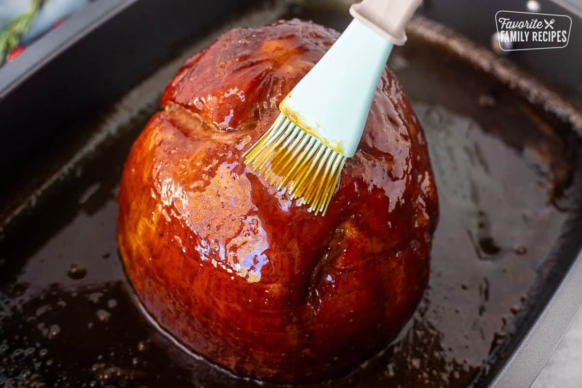Brushing Christmas ham with glaze in roasting pan.