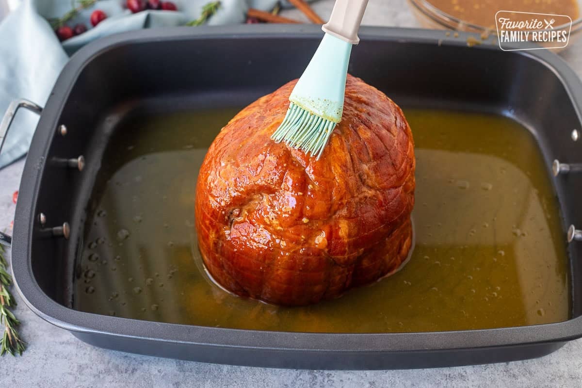 Brushing ham with seasoning glaze mixture in a roasting pan.