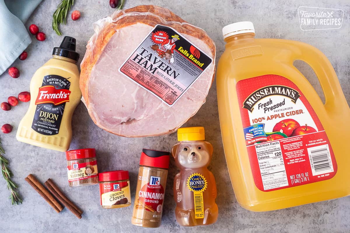 Ingredients to make Christmas Ham recipe including tavern ham, apple cider, honey, cinnamon, ground cloves, ground nutmeg, dijon mustard, cranberry sauce and cinnamon sticks.