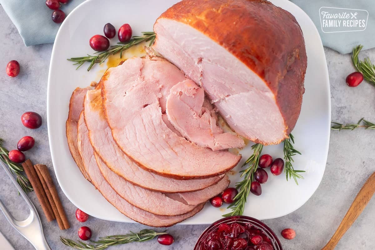 Sliced Christmas ham on a platter with cranberry sauce on the side.