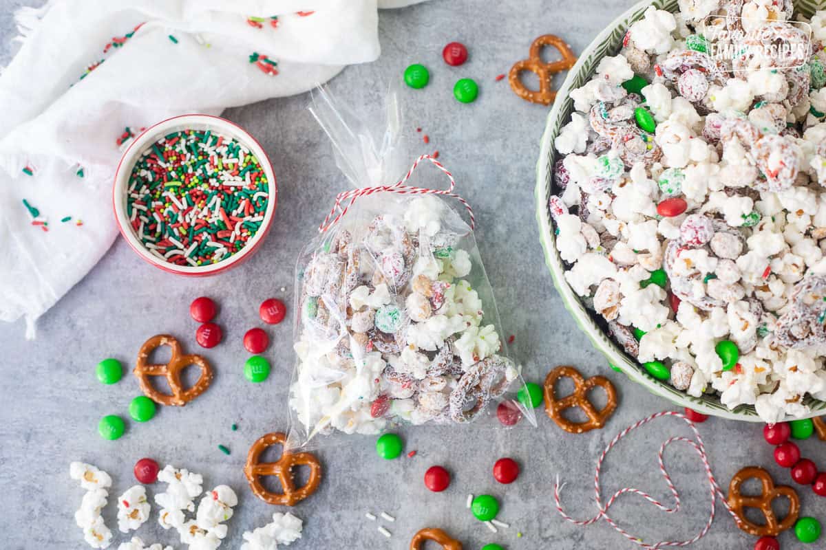 Christmas popcorn in a bag with a festive string tied at the top next to bowl of Christmas popcorn.