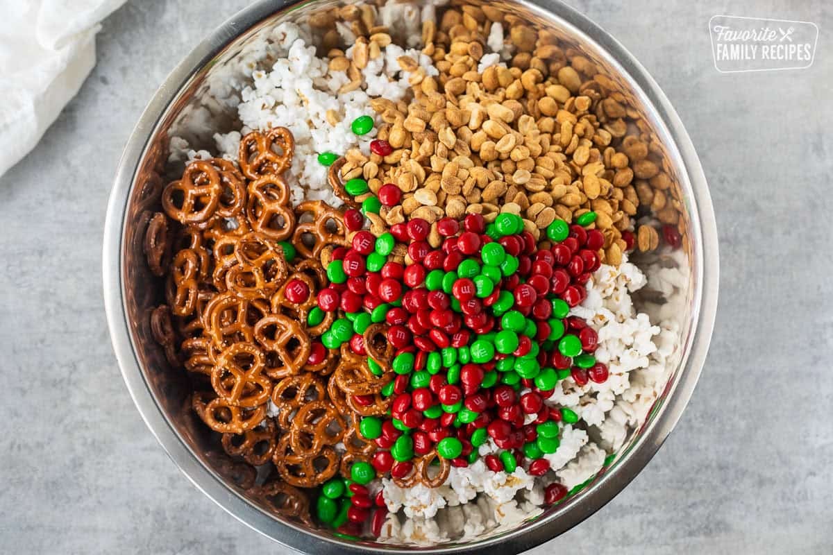 Large bowl of popcorn topped with pretzels, m&m's, roasted peanuts and mini pretzels.