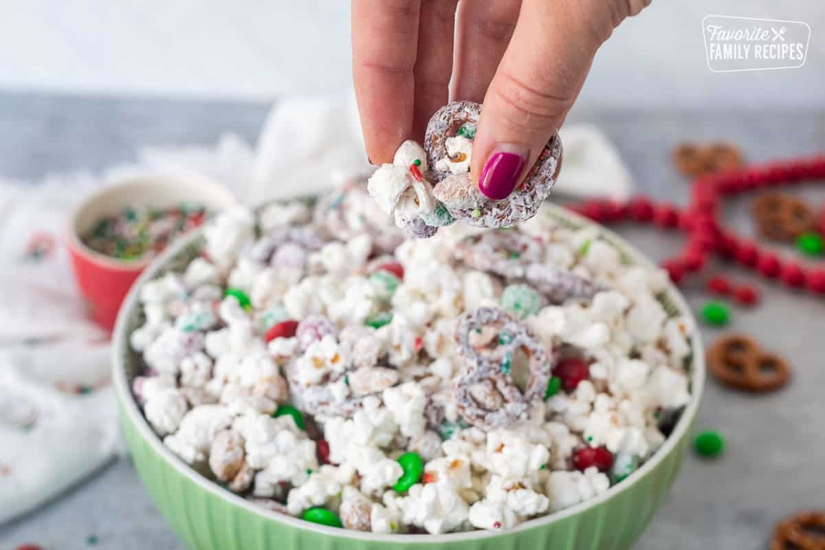 A hand picking up a bit of Christmas crunch popcorn from a large bowl.