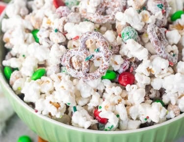 Bowl of Christmas popcorn with mini pretzels, red and green M&M's, roasted peanuts and festive sprinkles.