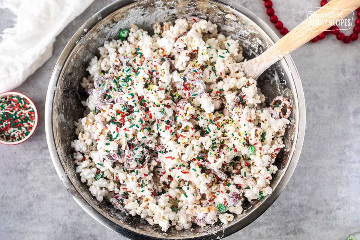 Sprinkles on top of mixed Christmas popcorn in a large mixing bowl with a spoon.