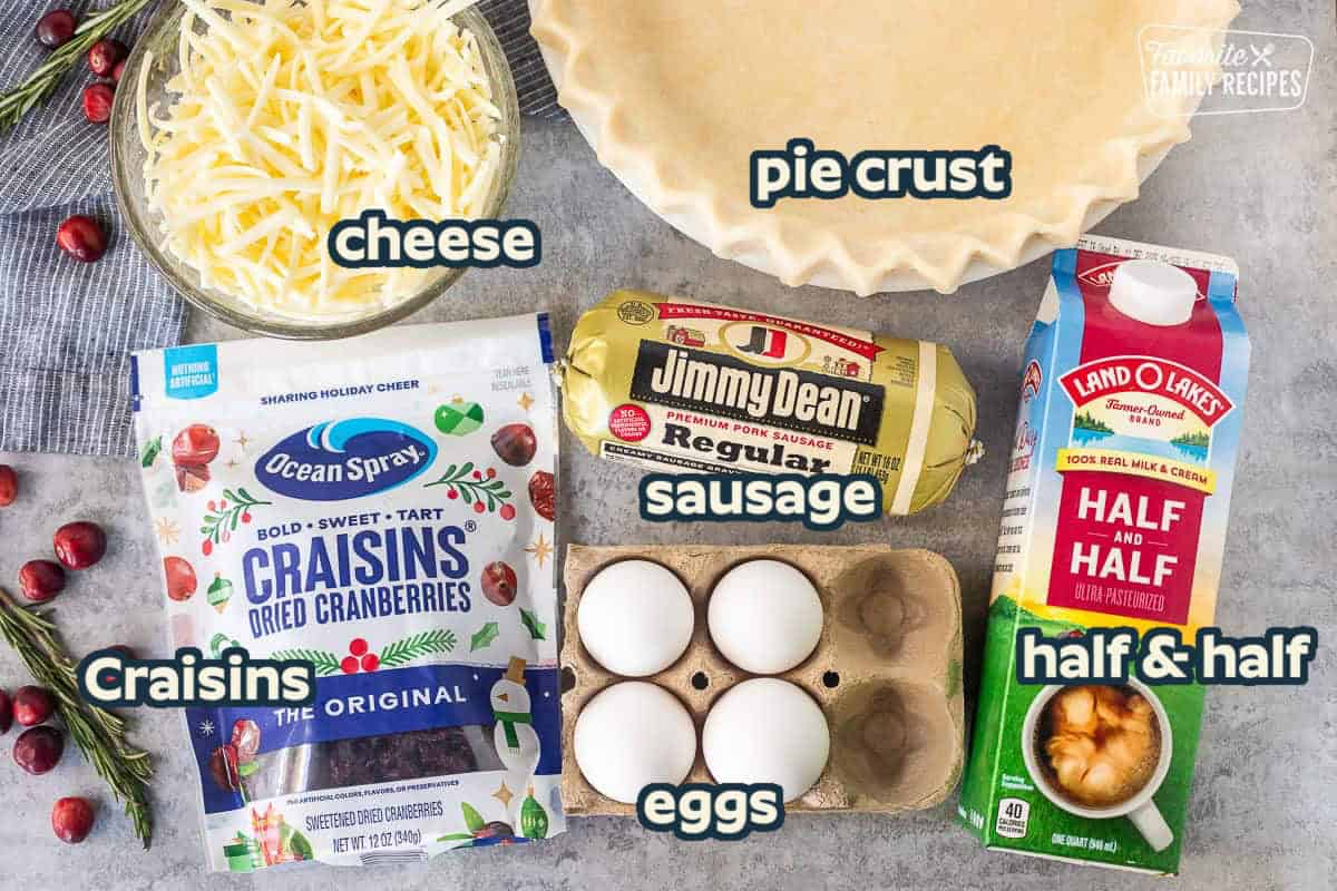 Ingredients to make Christmas Quiche including a pie crust, shredded Monterey Jack cheese, eggs, half and half, sausage, and dried cranberries.