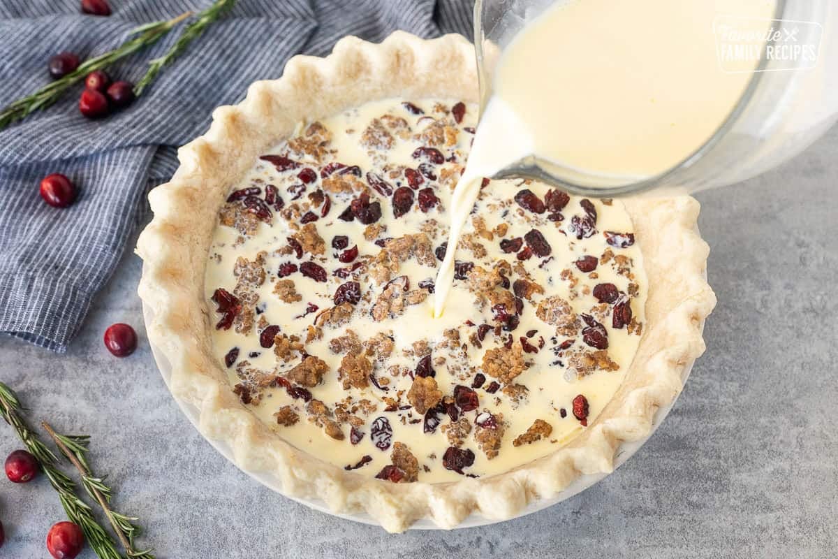 Pouring egg mixture into pie shell with sausage cheese and cranberries.