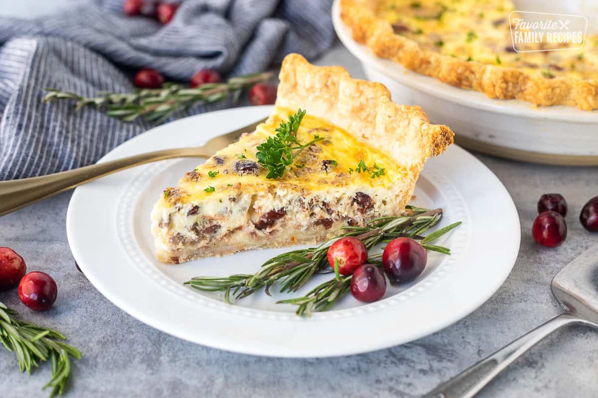 Slice of Christmas Quiche on a plate with rosemary and cranberries on the side.