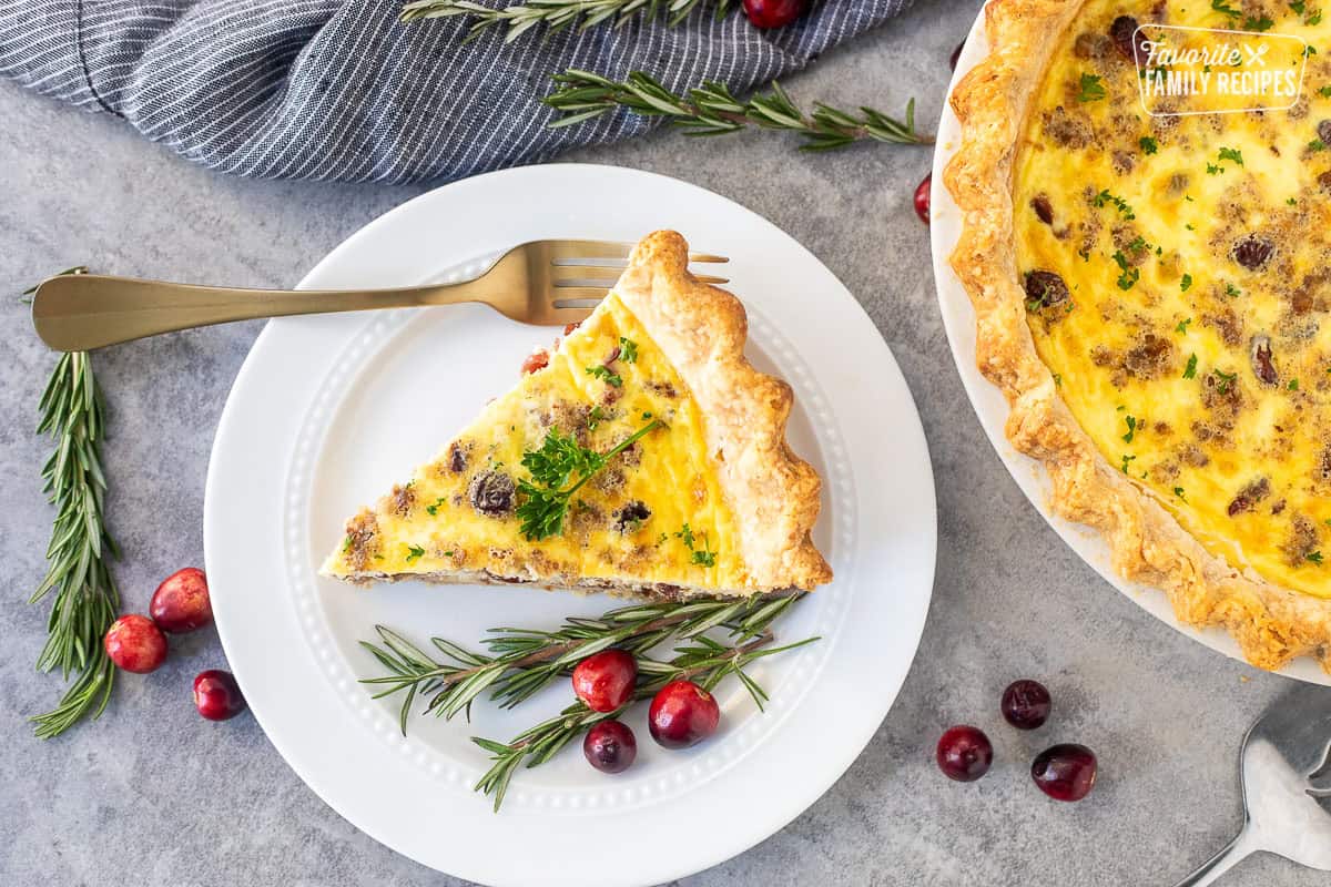 Slice of Christmas Quiche on a plate with rosemary and cranberries on the side.