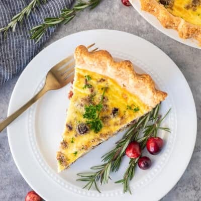 Slice of Christmas Quiche on a plate with rosemary and cranberries on the side.