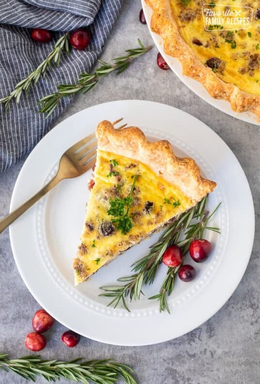 Slice of Christmas Quiche on a plate with rosemary and cranberries on the side.