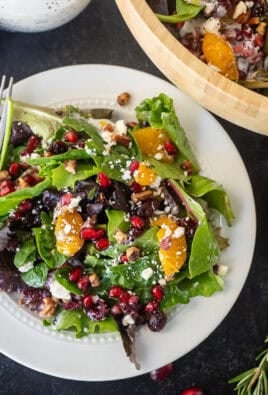 Plate with a serving Christmas salad of spring mix, feta, candied pecans, pomegranate, mandarin oranges, dried cranberries and poppyseed dressing.
