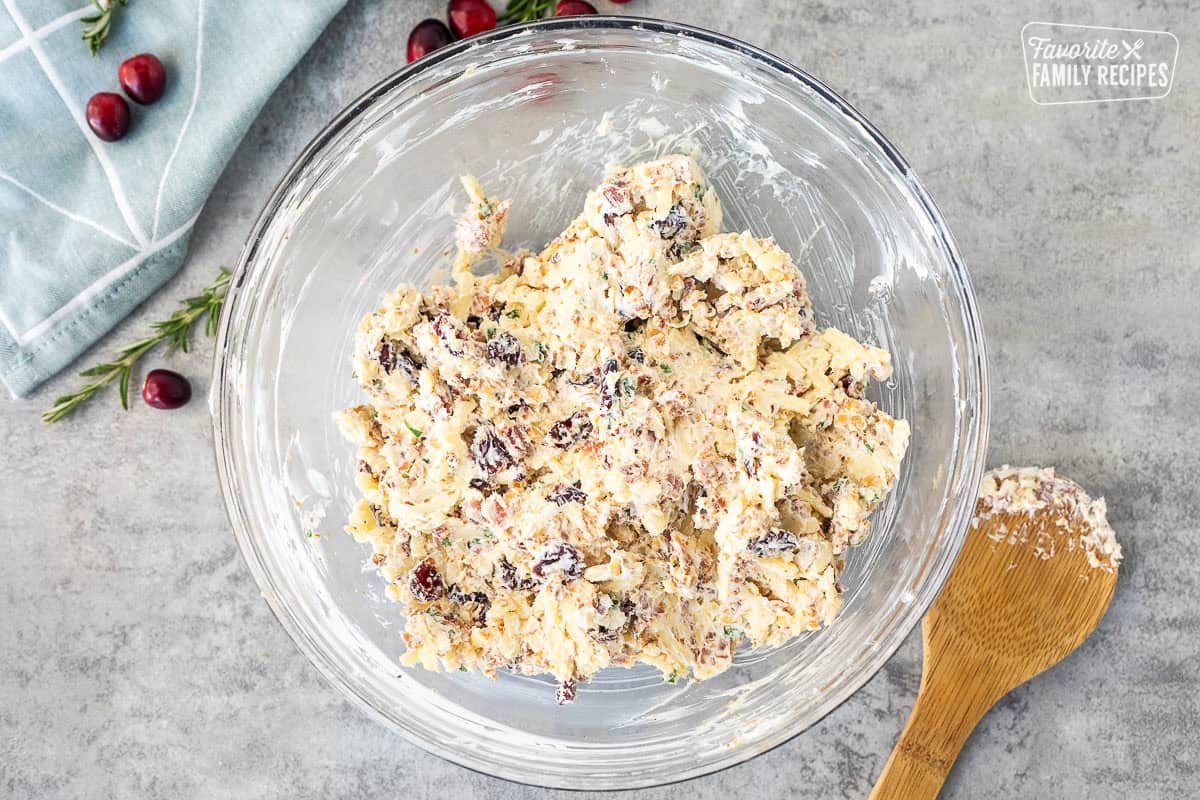 Combined cranberry cheese bowl ingredients in a glass mixing bowl. Wooden spoon on the side.