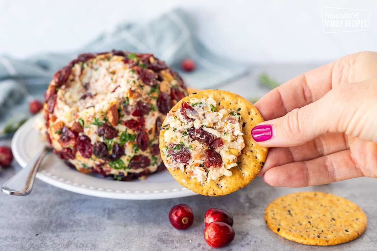 Hand holding a cracker with cranberry cheese ball spread on top.