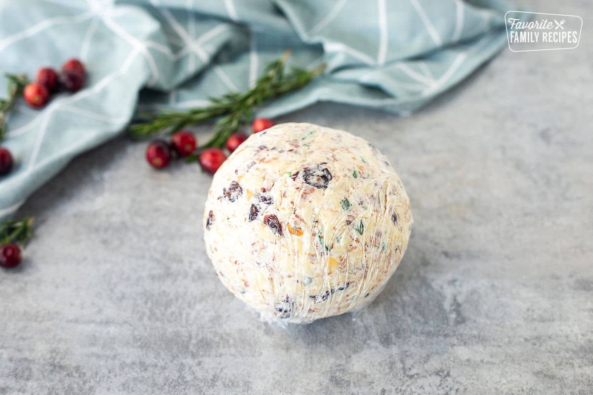 Round shaped cranberry cheese ball in plastic wrap.