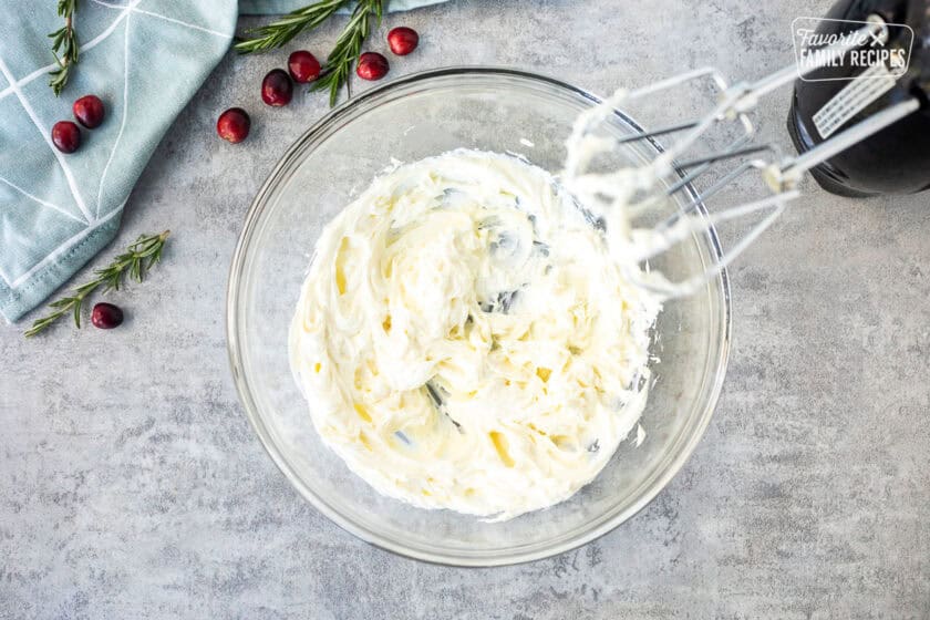 Glass mixing bowl with whipped cream cheese and electric beaters.