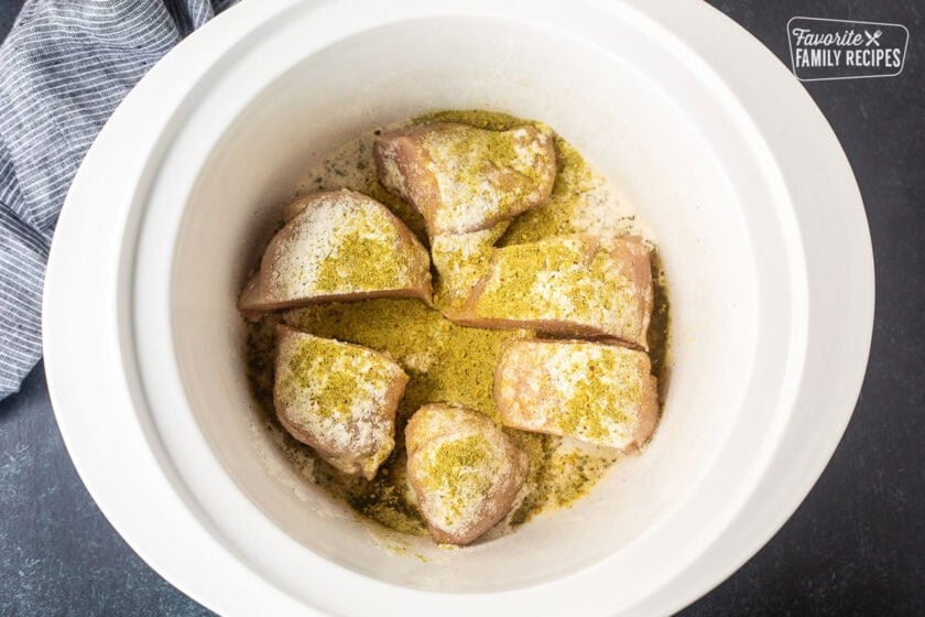 Sliced chicken breast in a crock pot sprinkled with seasonings.