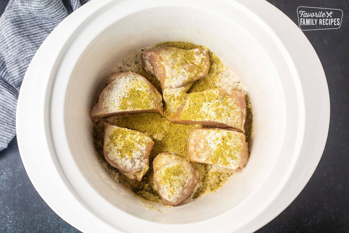 Sliced chicken breast in a crock pot sprinkled with seasonings.
