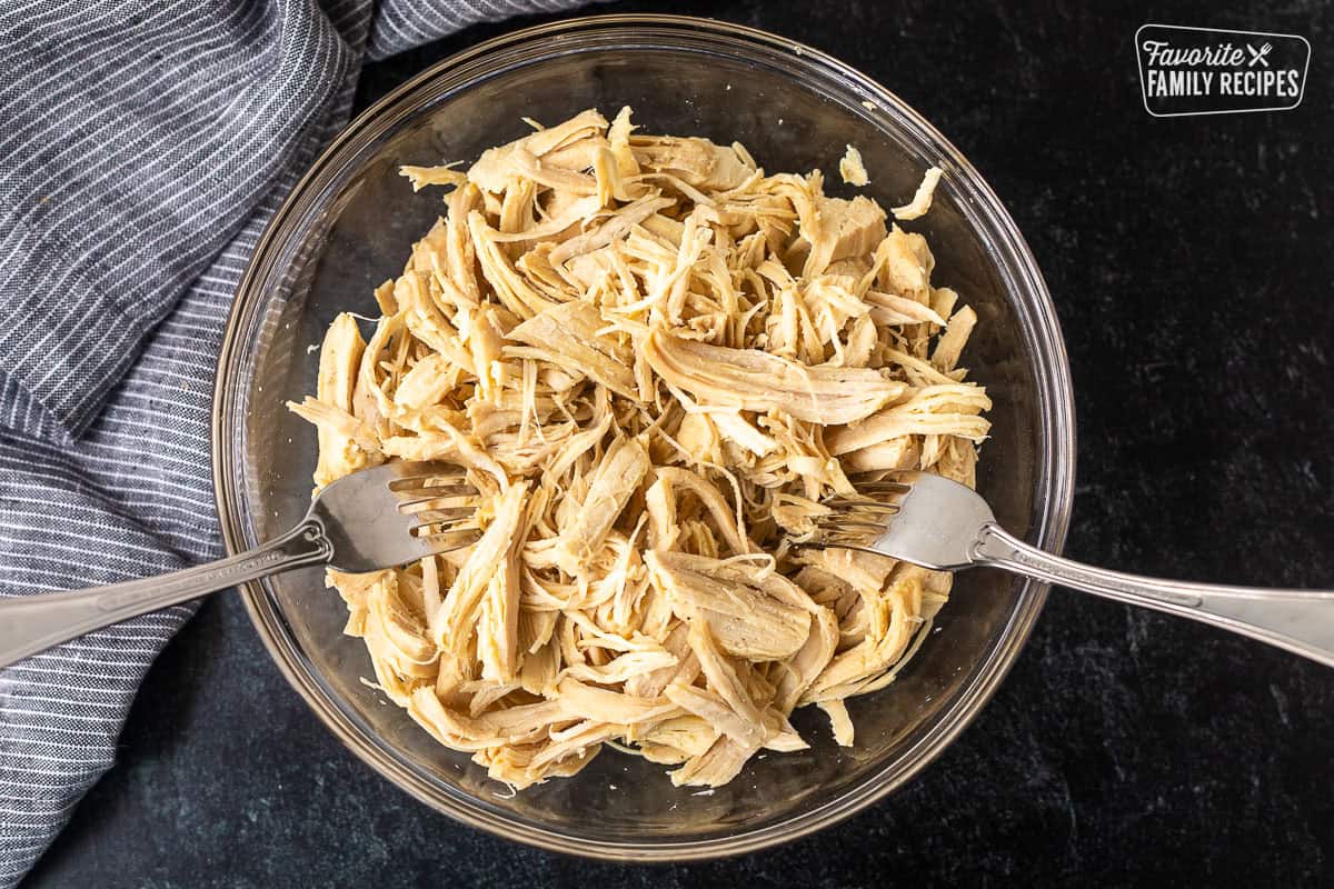 Bowl with shredded chicken and two forks.