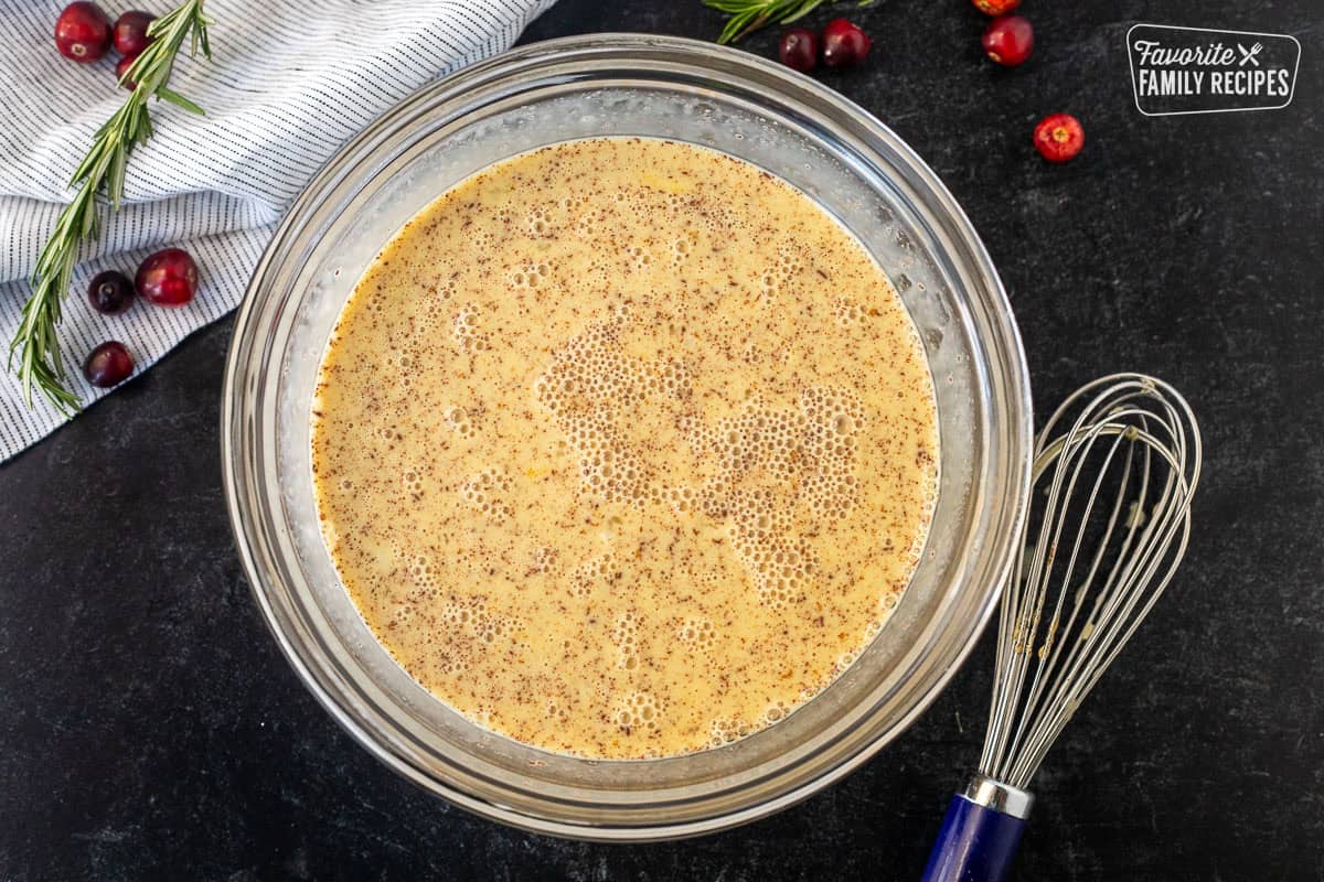 Glass bowl with egg mixture and whisk on the side.