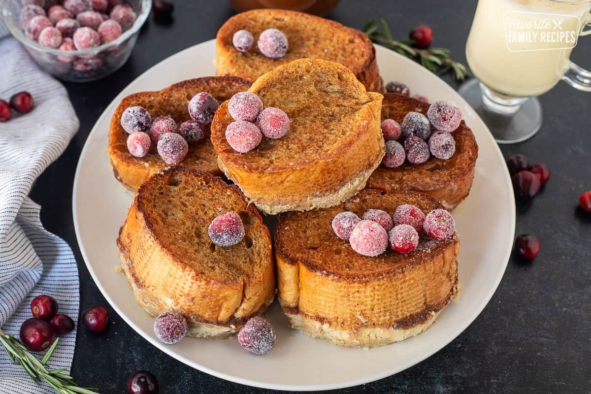 This Eggnog french toast with gingerbread syrup is my new favorite Christmas breakfast. Get a taste of Christmas in every gooey, delicious bite! This post is sponsored by Meadow Gold® Dairy and Dairy Farmers of America Slices of eggnog French toast on a plate garnished with sugared cranberries.