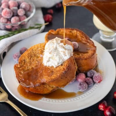 Pouring gingerbread syrup on top of two slices of eggnog French toast with whipped cream.