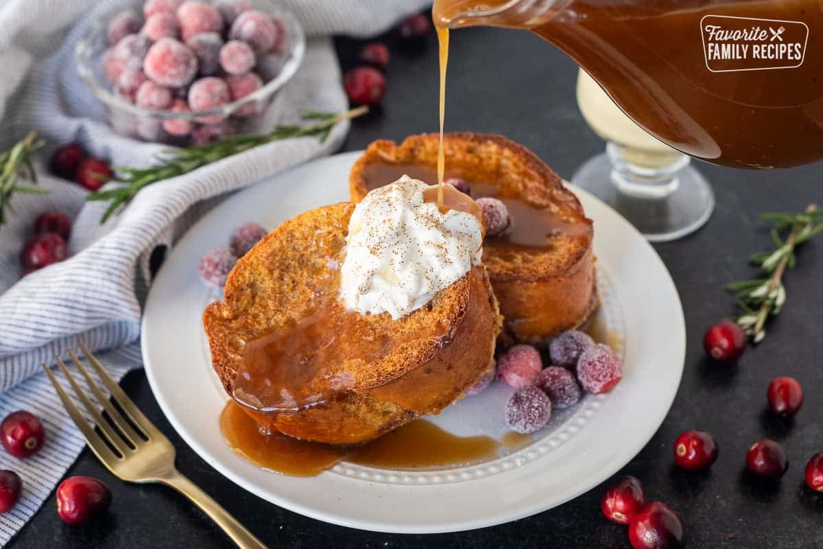 This Eggnog french toast with gingerbread syrup is my new favorite Christmas breakfast. Get a taste of Christmas in every gooey, delicious bite! This post is sponsored by Meadow Gold® Dairy and Dairy Farmers of America Pouring gingerbread syrup on top of two slices of eggnog French toast with whipped cream.