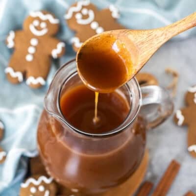 Wooden spoon drizzling gingerbread syrup into glass pitcher.
