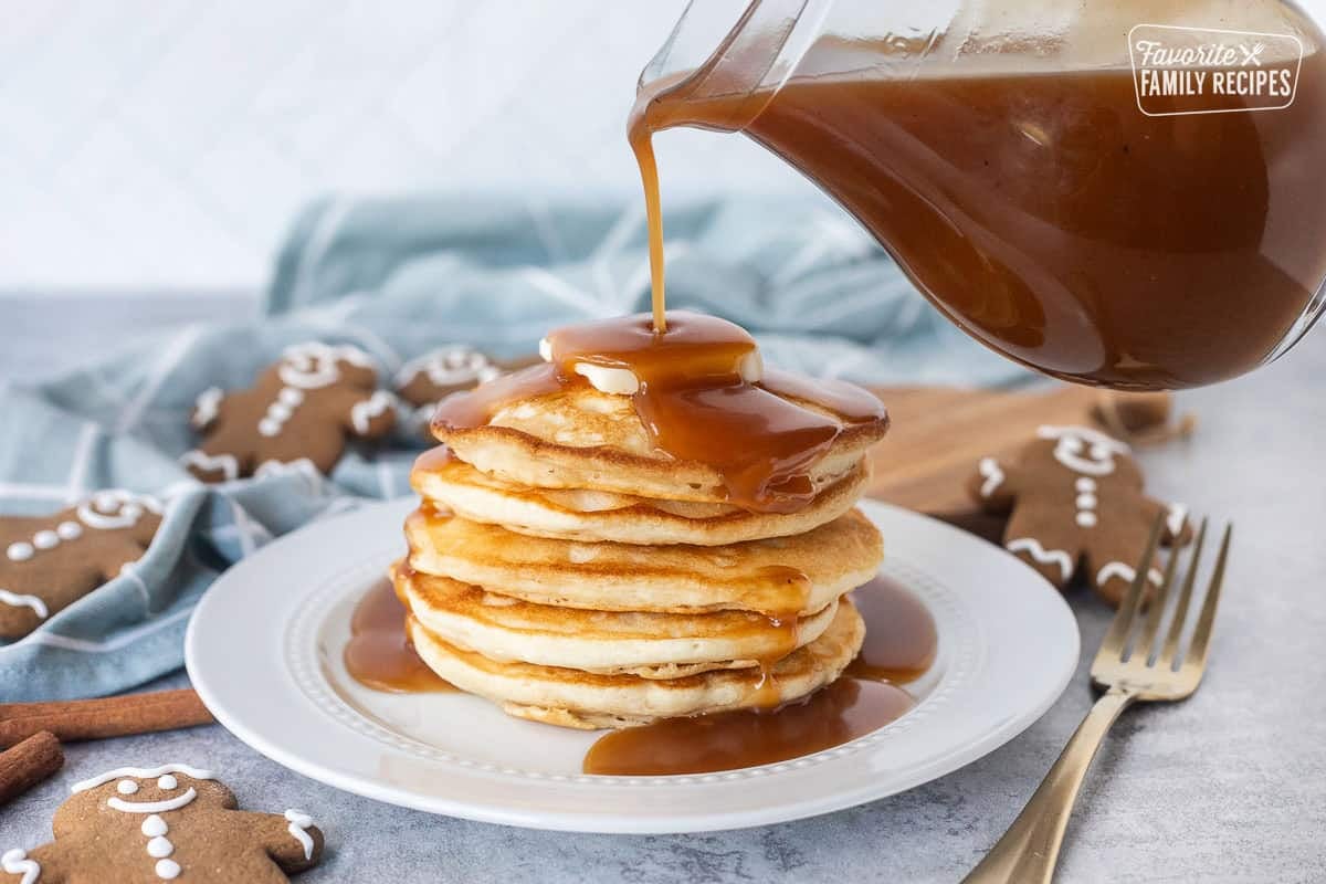 Pouring gingerbread syrup over a stack of pancakes on a plate.