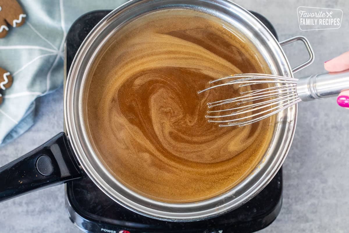 Stirring hot gingerbread syrup in a saucepan with a whisk over an electric burner.