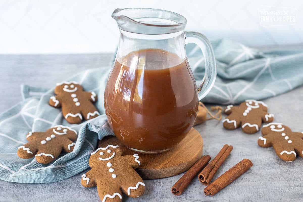 Gingerbread syrup in a glass pitcher. Gingerbread man cookies and cinnamon sticks on the side.