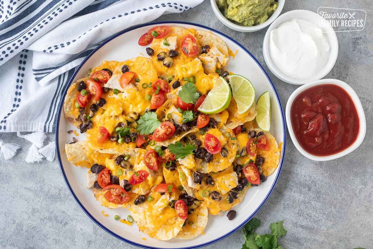 Plate with oven nachos garnished with tomatoes, cilantro and green onions. Sides of sour cream, guacamole and salsa.