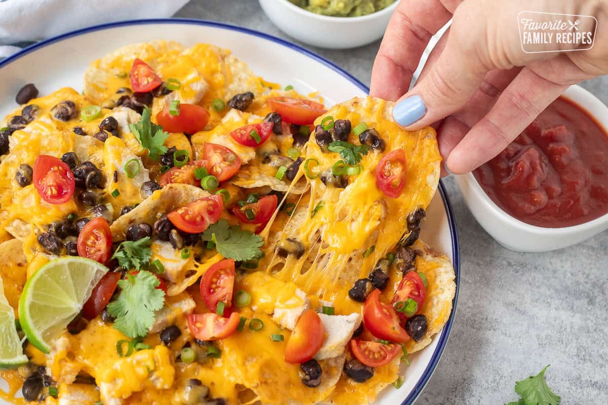 Hand pulling up a cheesy oven nacho from a plate.