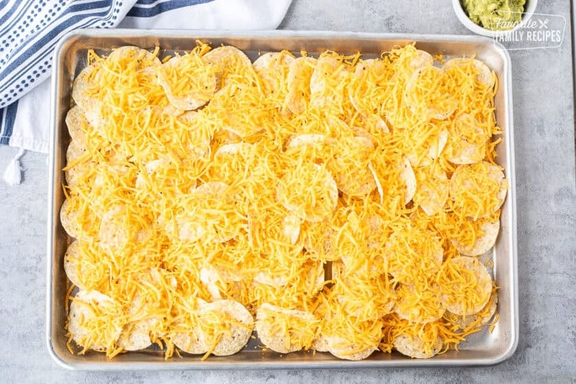 Sheet pan of tortilla chips topped with shredded cheddar cheese.