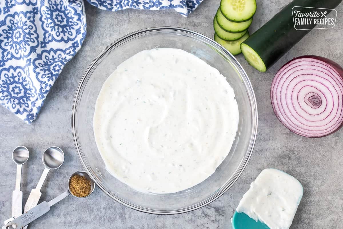 Glass bowl with Raita mixed and spatula on the side.