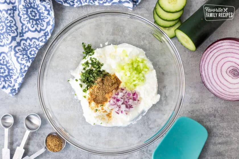 Glass bowl with plain yogurt, red onion, cumin, cucumber and cilantro.
