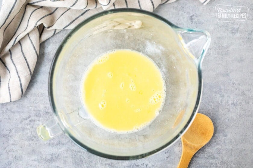 Glass mixing bowl with milk and melted butter. Wooden spoon on the side.