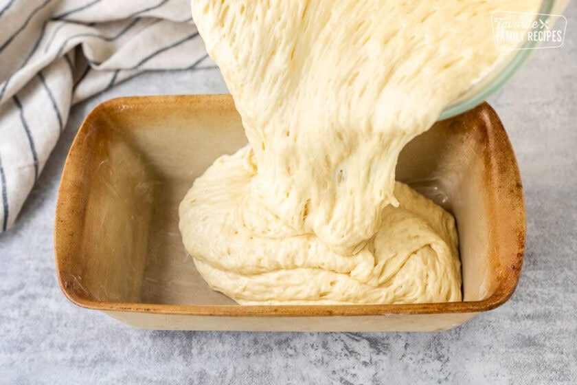 Pouring Sally Lunn Bread dough into greased loaf pan.