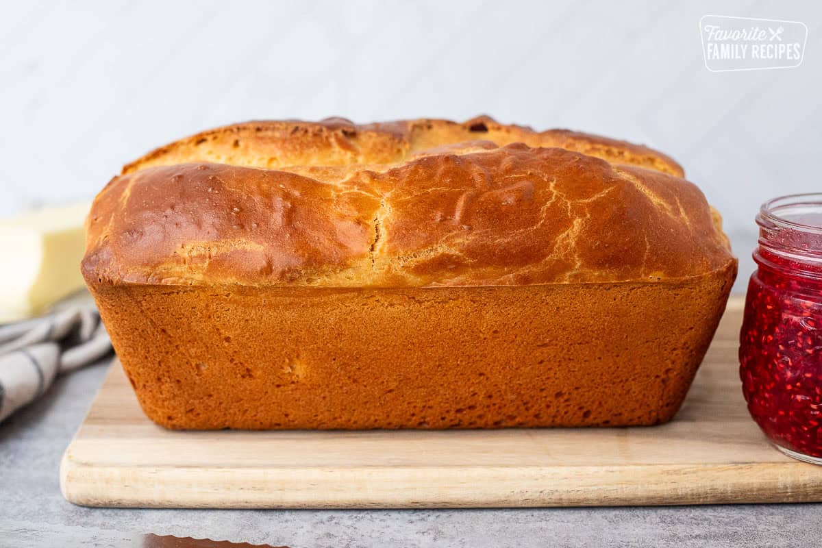 Loaf of Sally Lunn Bread on wooden board. Butter dish and raspberry jam on the side.