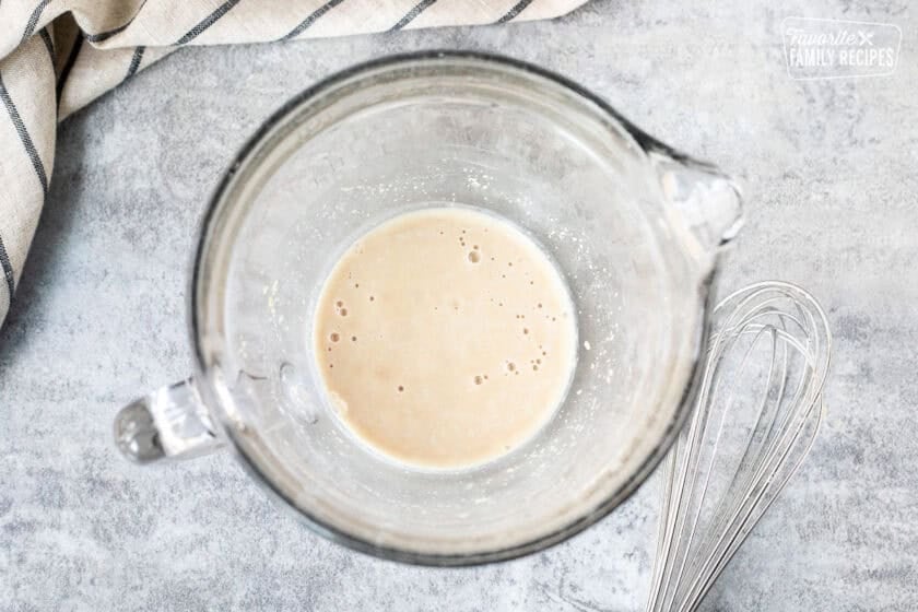 Glass bowl with activated yeast. Whisk on the side.