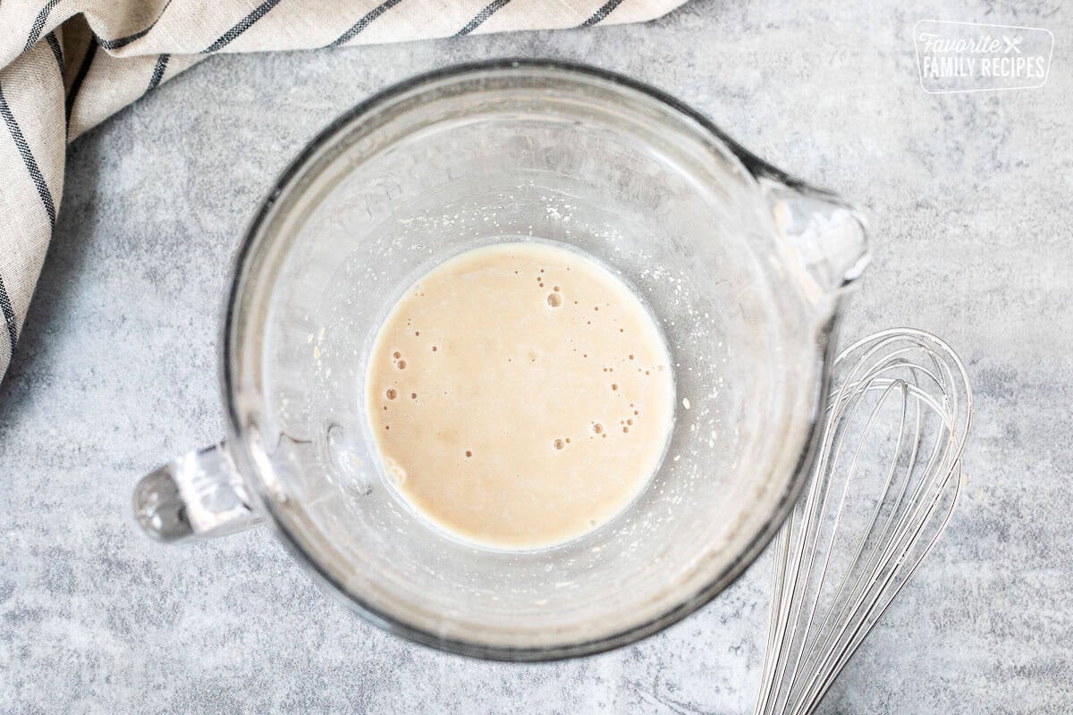 Glass bowl with activated yeast. Whisk on the side.