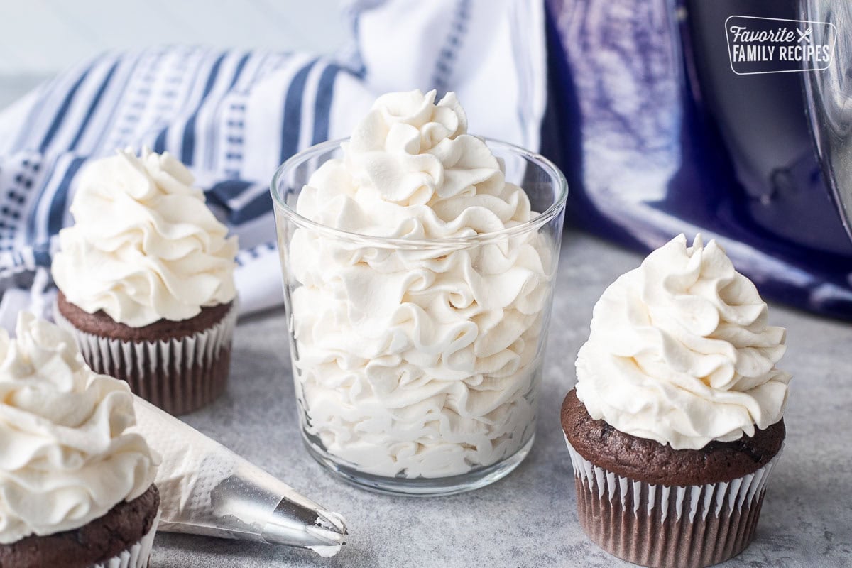 Glass with piped stabilized whipped cream frosting next to cupcakes.