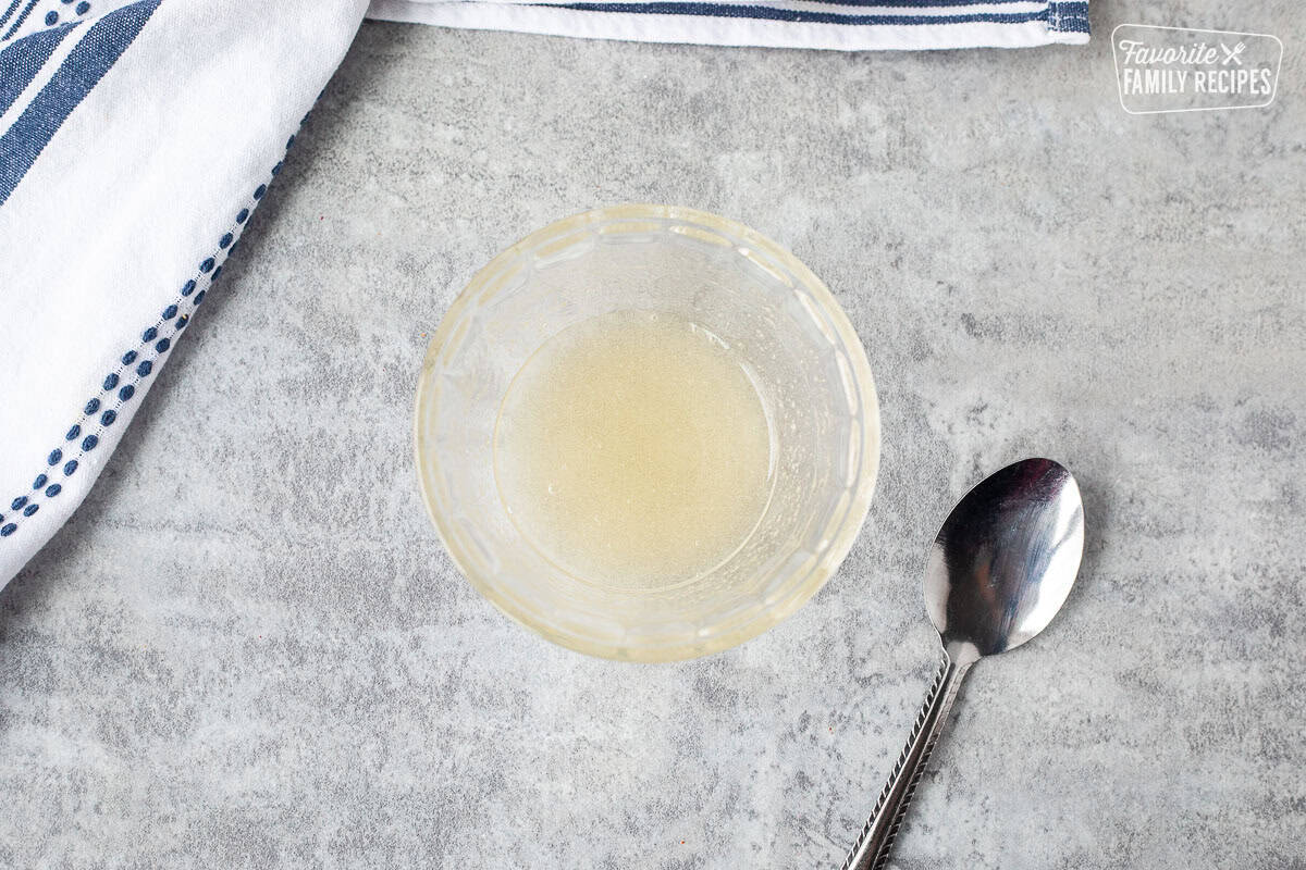 Liquid gelatin in small glass bowl with spoon on the side.
